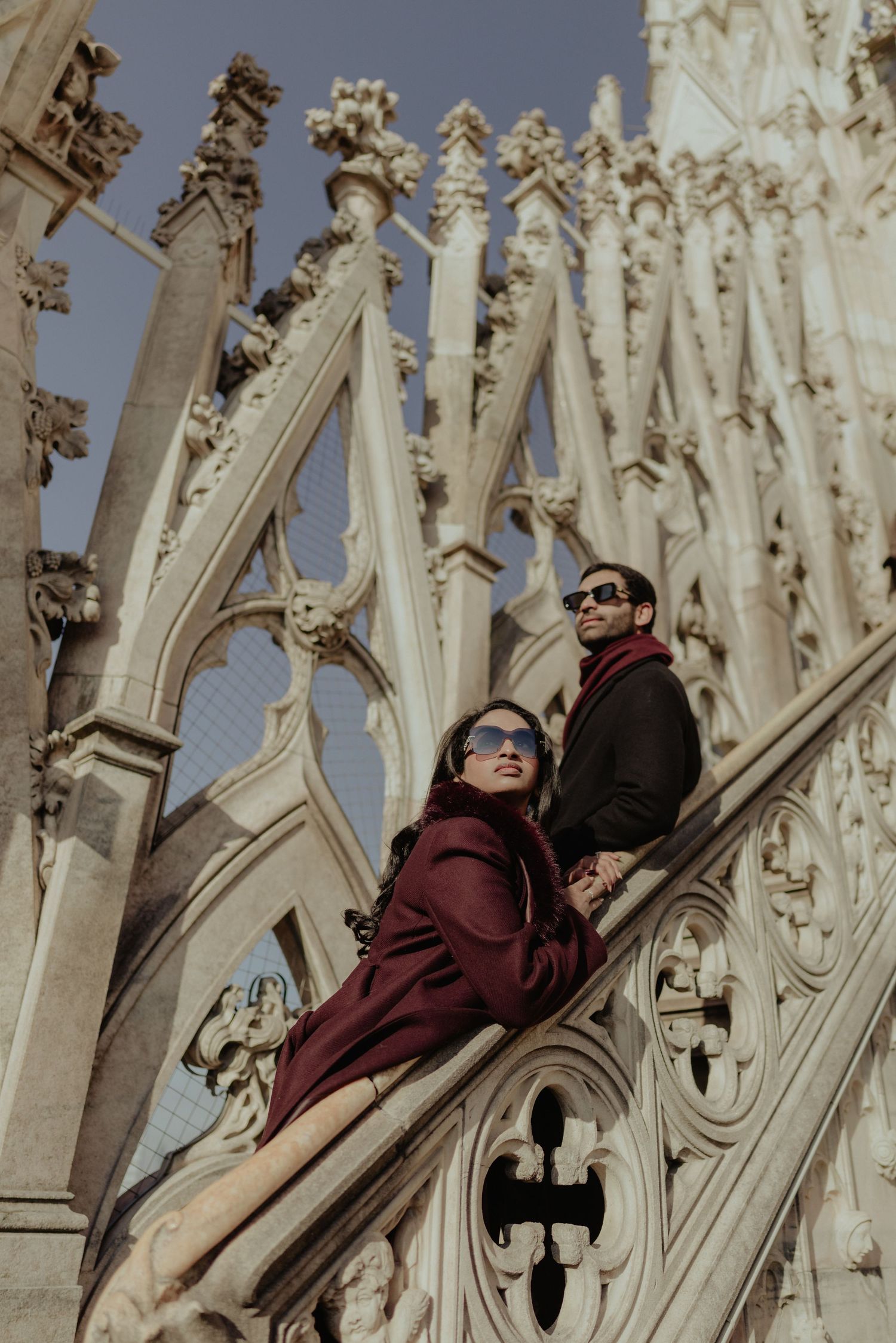 Couple in sunglasses posing on the ornate Gothic spires of Milan Cathedral rooftop on a sunny day.
