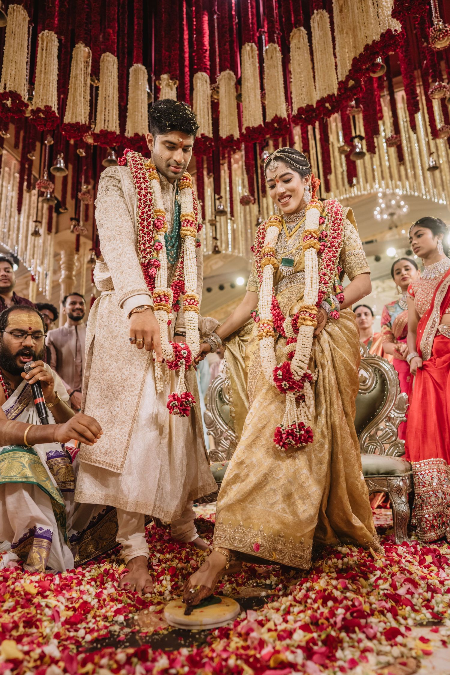 Indian bride and groom performing traditional wedding rituals, adorned in gold attire and floral garlands at a decorated mandap.