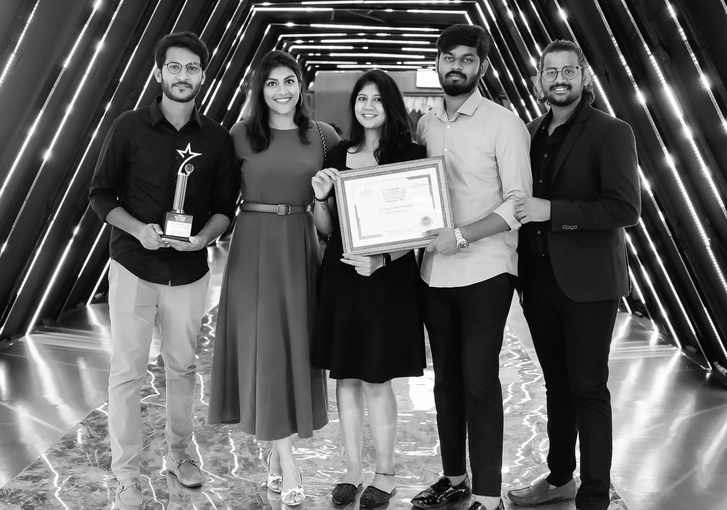 Group of five professionals posing with award trophy and certificate at formal recognition ceremony.
