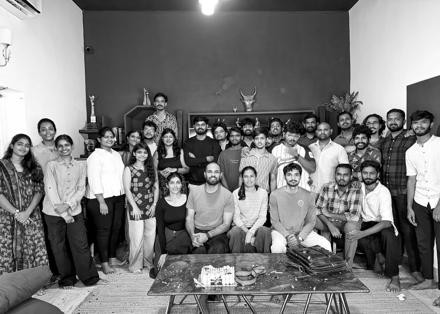 Large group of young professionals posing together indoors for a black and white team photo.