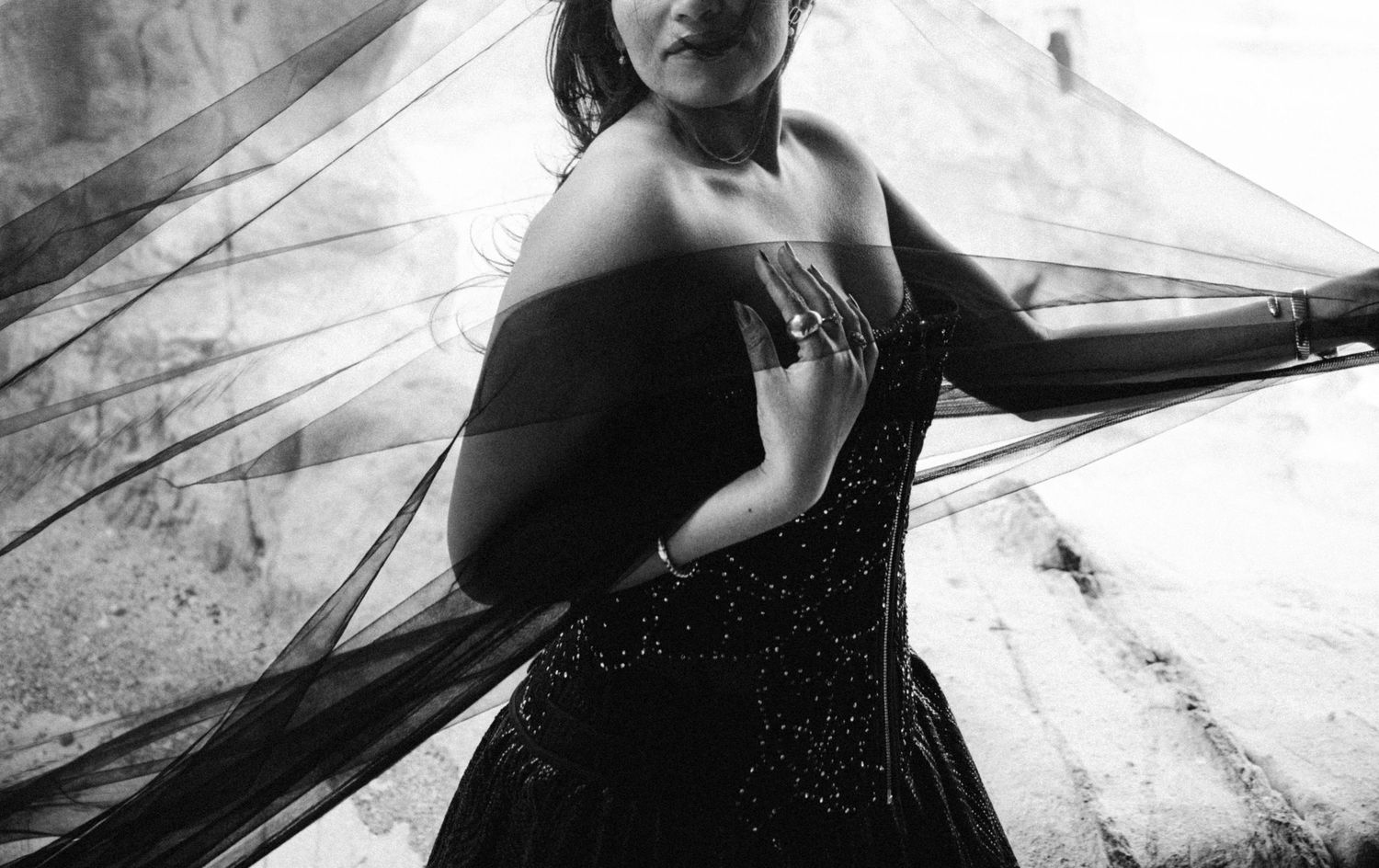 Black and white photo of a woman in a strapless beaded gown with flowing sheer fabric draped elegantly around her.