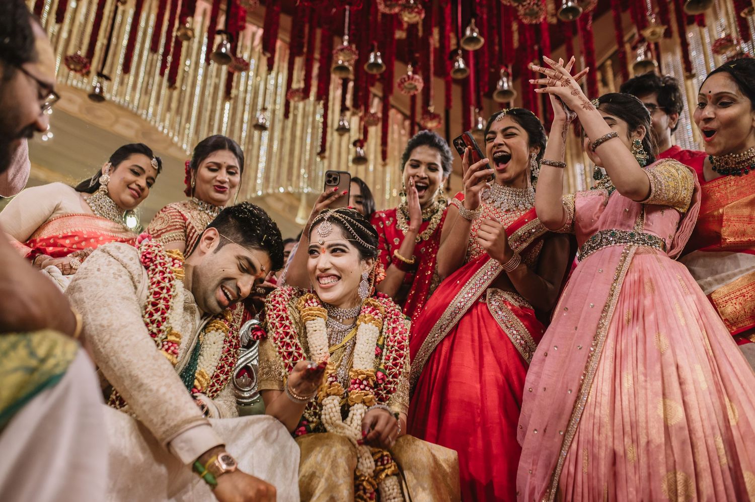 Joyful South Indian wedding ceremony with bride in red saree, groom, and celebrating bridesmaids adorned in traditional attire.