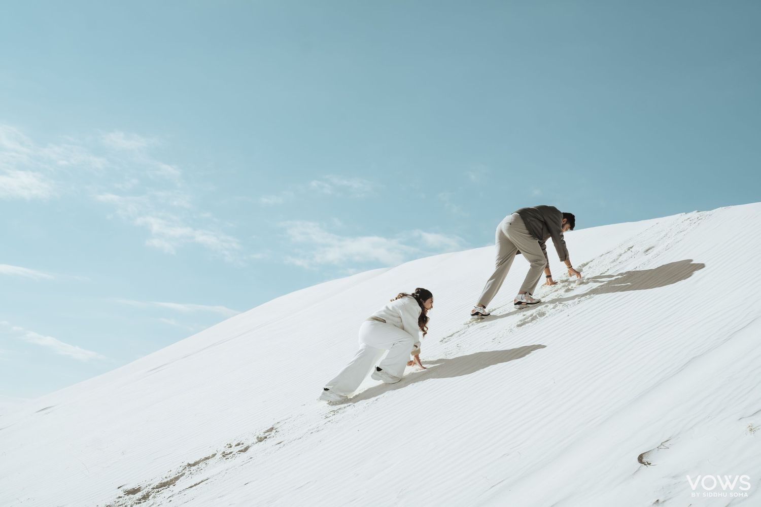 Two people climbing a steep snow-covered hill under a clear blue sky in winter.