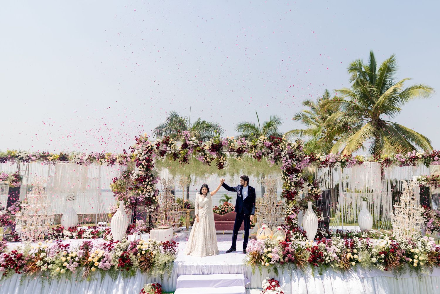A joyful couple celebrates under a shower of confetti at an elegant floral wedding ceremony outdoors.