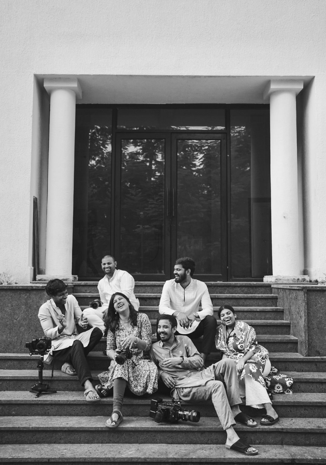 Black and white photo of a joyful group of friends laughing and relaxing on building steps.