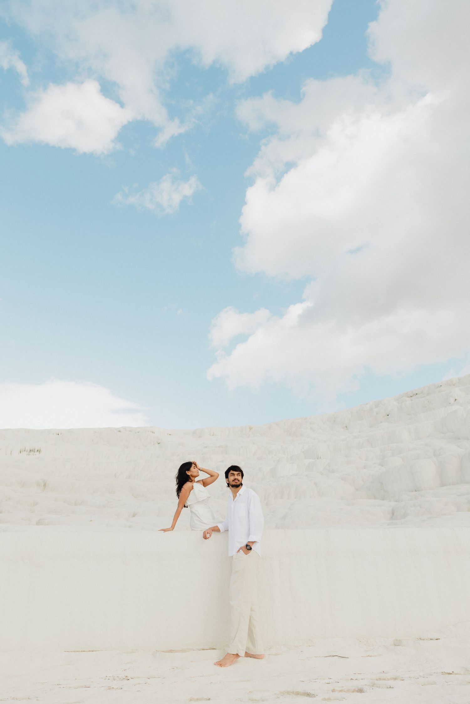 Couple dressed in white posing at Pamukkale travertine terraces under blue sky.