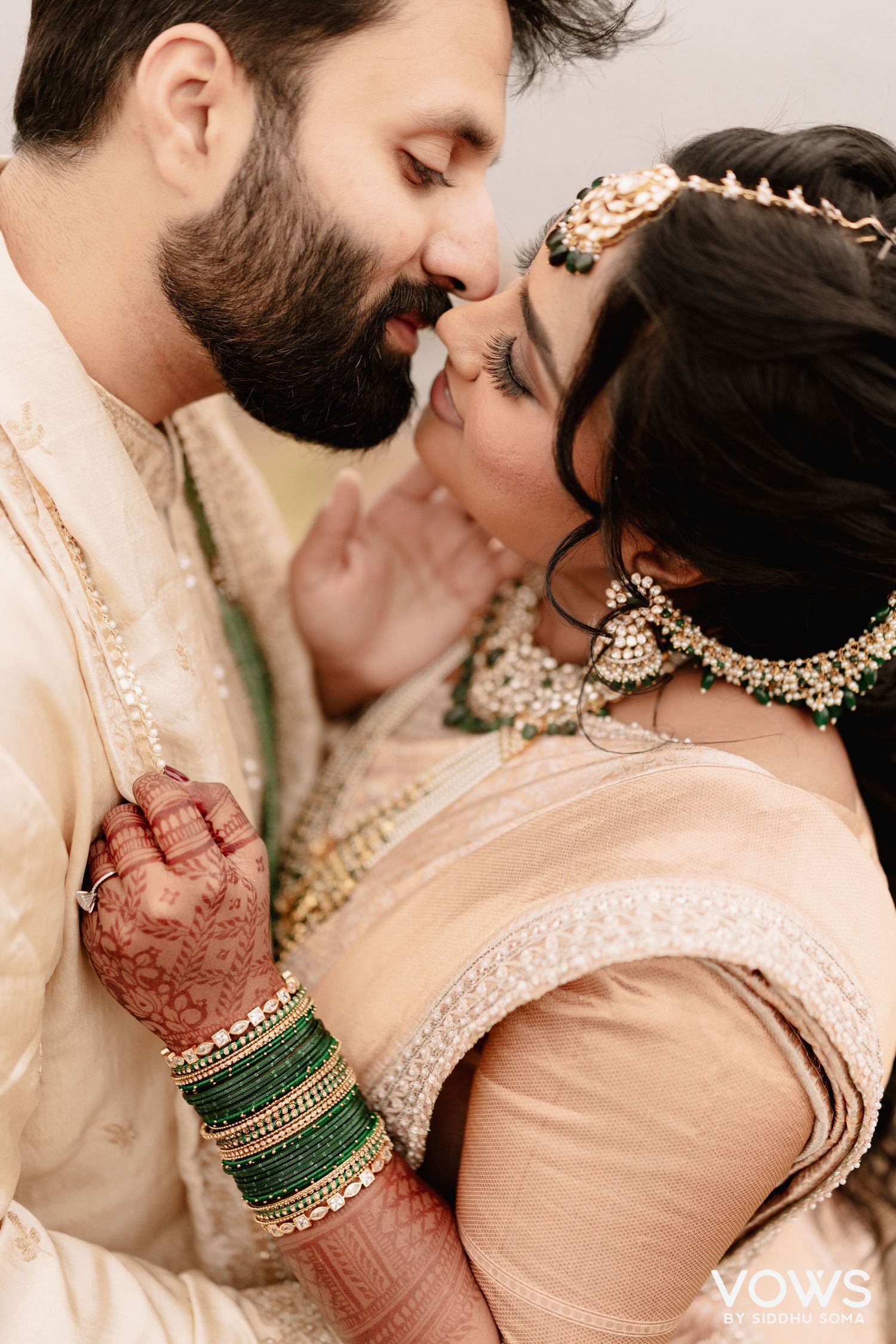 Indian bride and groom in traditional attire share a romantic moment, bride wearing green bangles and gold jewelry.