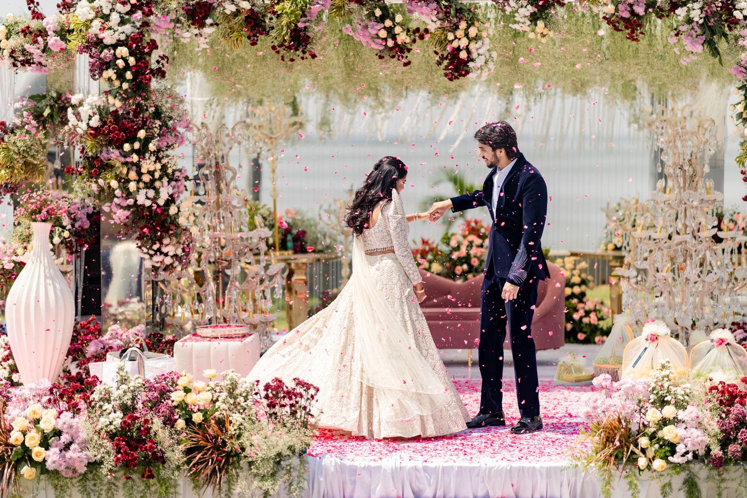 Bride and groom sharing a magical moment on a floral-decorated wedding stage surrounded by pink and white blooms.