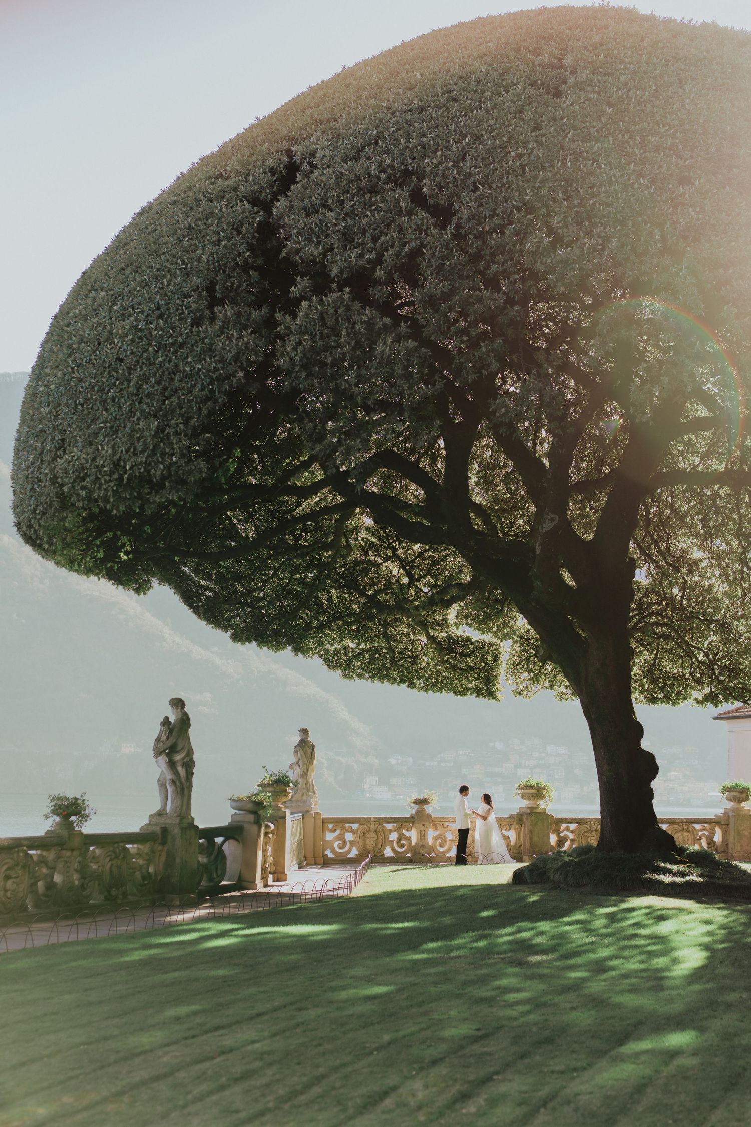 Couple exchanging vows under a large umbrella tree on an elegant Italian villa terrace overlooking Lake Como.
