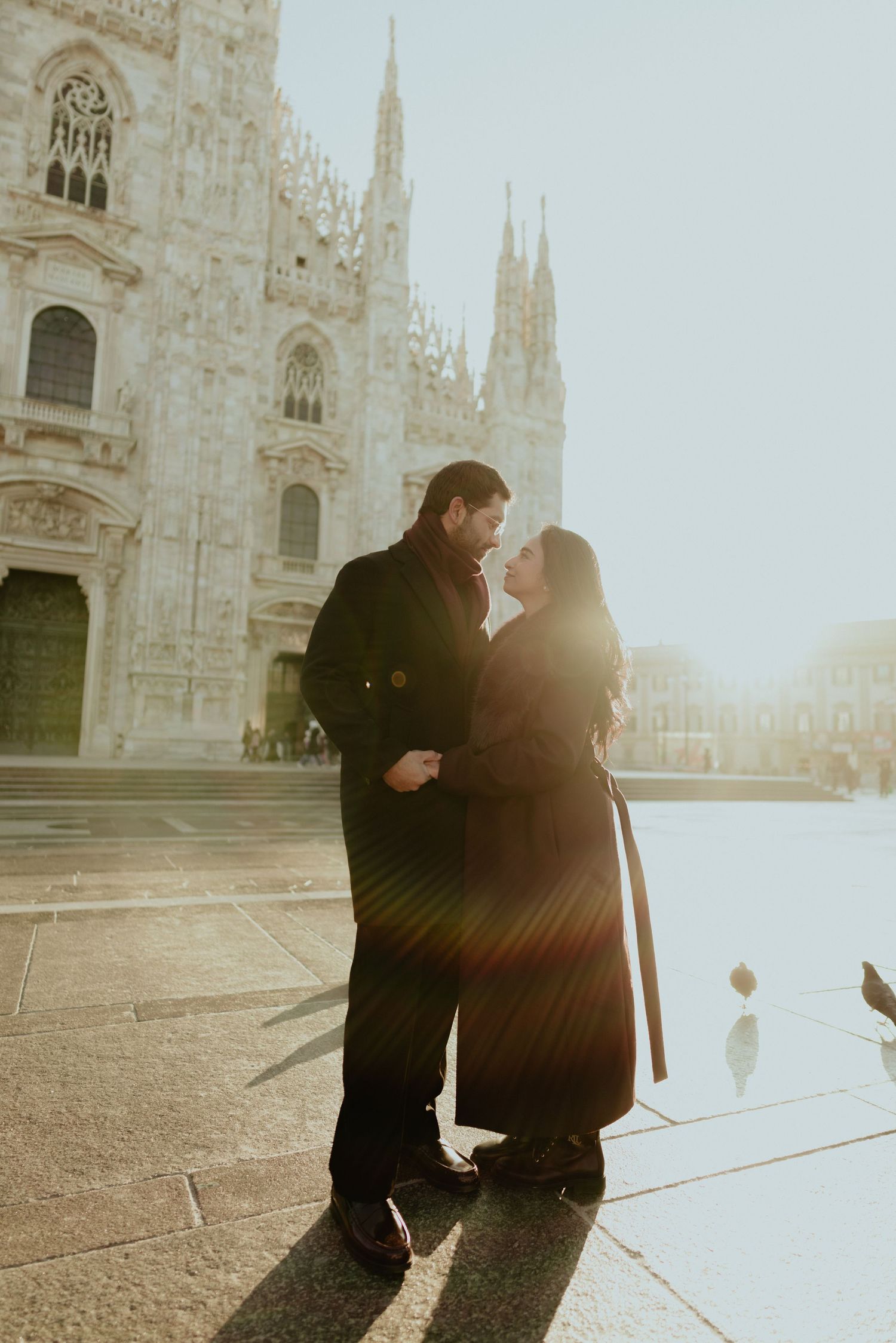 Couple sharing a romantic moment with golden sun flare in front of Milan's Duomo.
