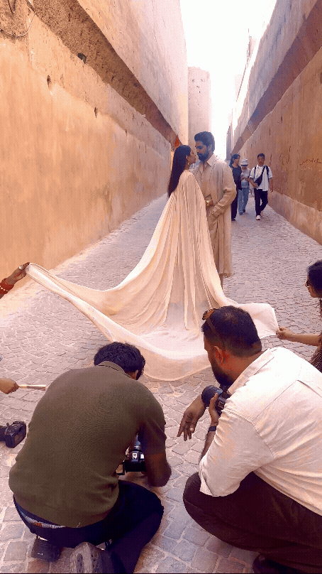 Photographers capture a couple in elegant cream attire posing in a narrow alley with ancient sandstone walls.