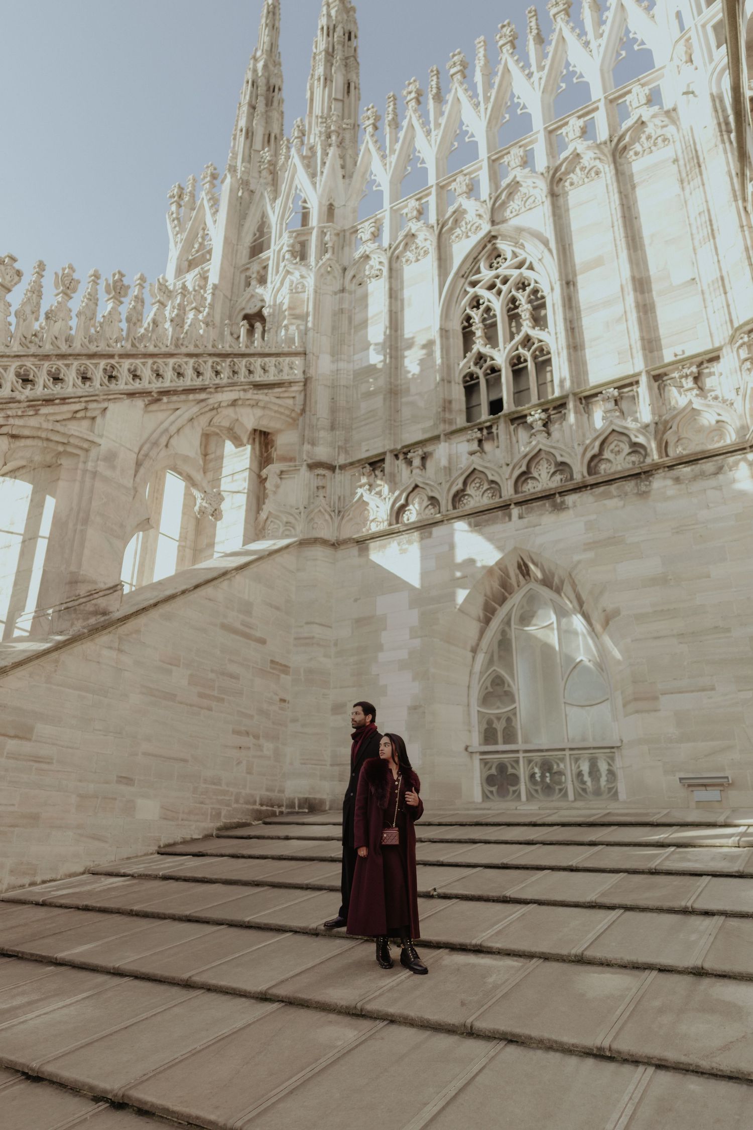 A couple in dark formal wear poses on the steps of Milan's ornate Gothic Duomo cathedral.