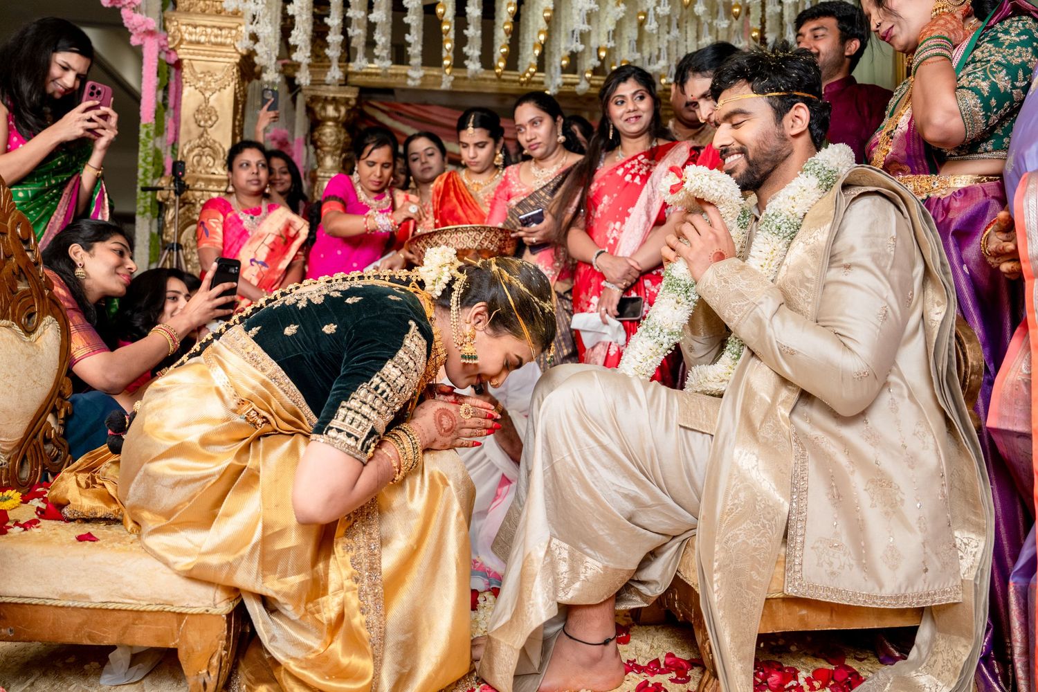 Vibrant South Indian wedding ceremony with bride in gold saree bowing to groom surrounded by colorful guests.