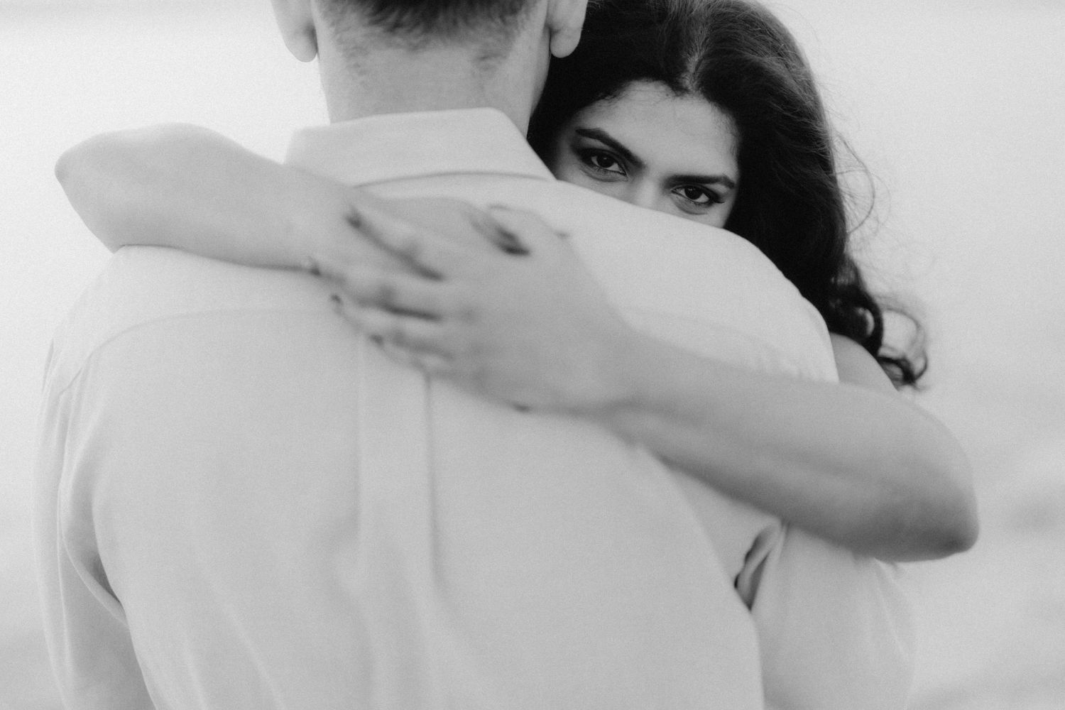 Black and white photo of a couple embracing, woman with dark hair looking over mans shoulder.