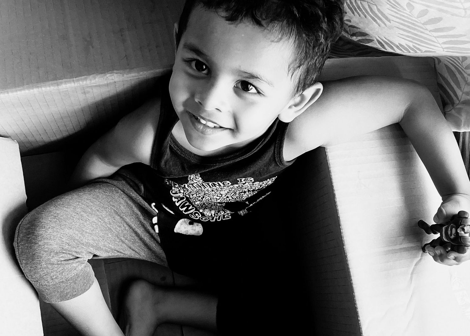 Black and white photo of a smiling young boy relaxing on a couch holding a remote control.