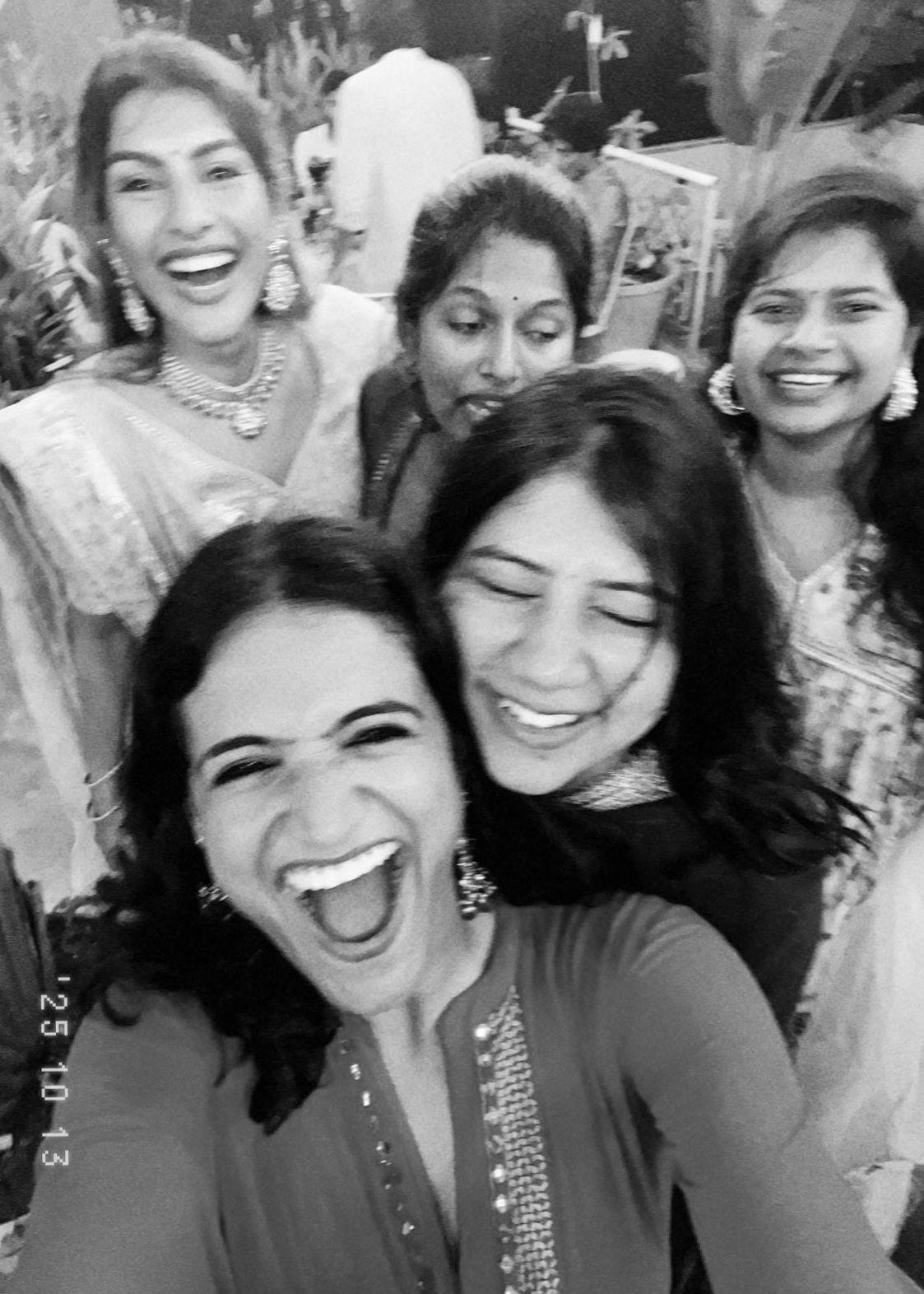 Black and white selfie of five joyful women in traditional Indian attire laughing together at a celebration.