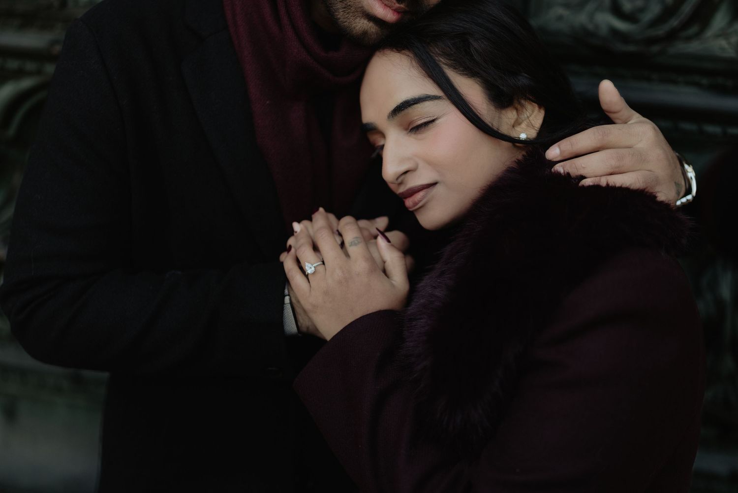Intimate couple embrace, woman in burgundy fur coat with eyes closed, man tenderly holding her shoulders.