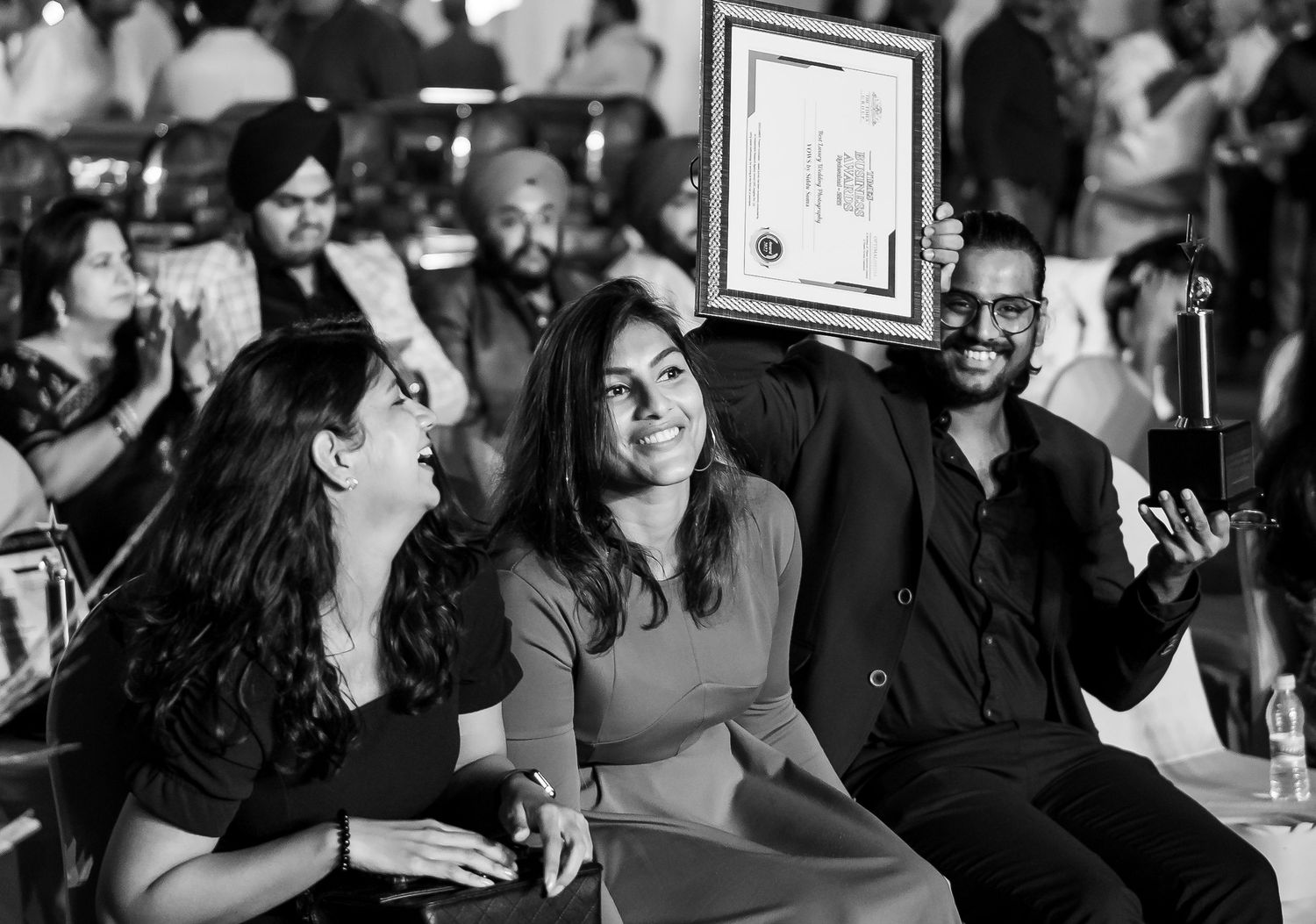 Three people smile and pose with a framed certificate at an awards ceremony in a black and white photo.
