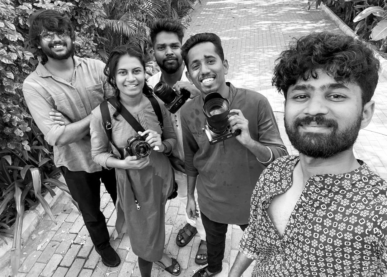 Group of five young photographers posing for a selfie outdoors, holding cameras, in black and white photo.