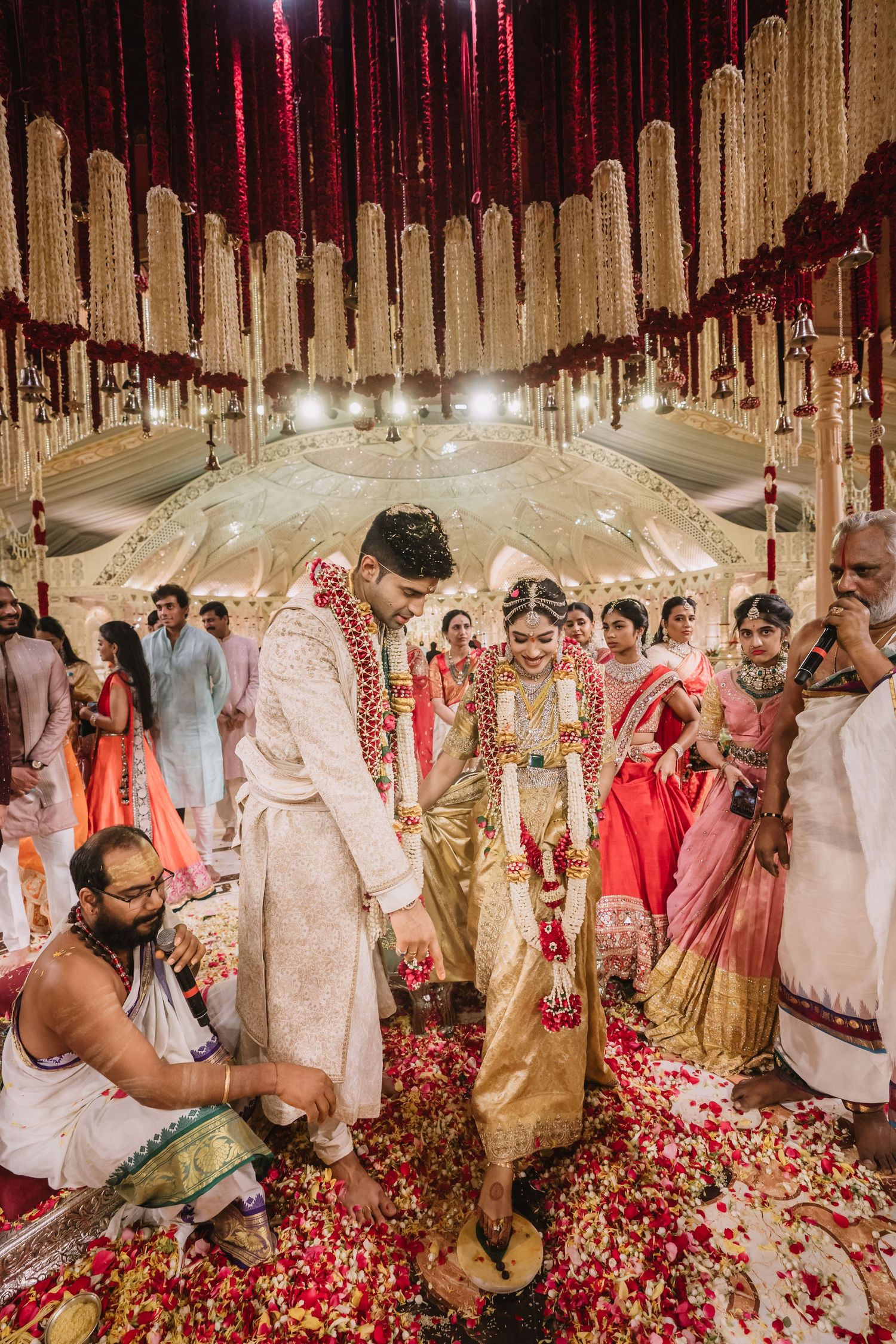Indian bride and groom perform traditional Hindu wedding ceremony under floral mandap with rose petals.