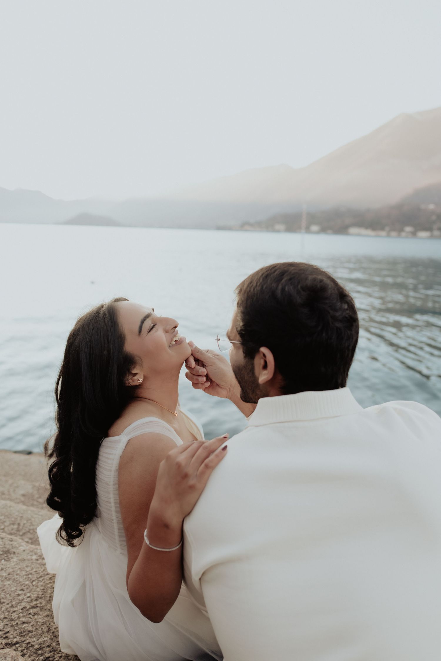 Couple sharing a romantic moment by a serene lake with mountain views in the background.