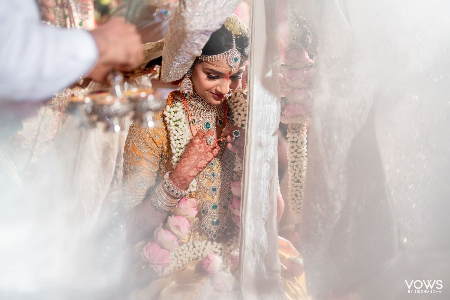 Indian bride in golden lehenga with mehndi hands during traditional wedding ceremony under white veil.