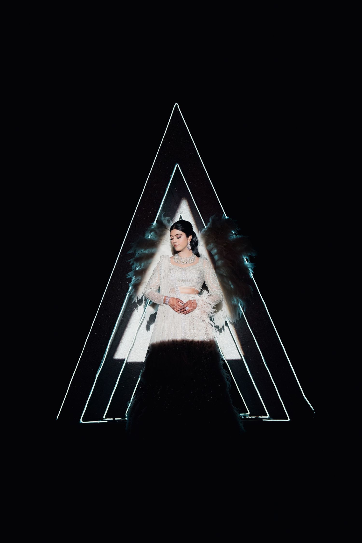 Woman in white dress stands centered within glowing triangular neon light frame against dark background.