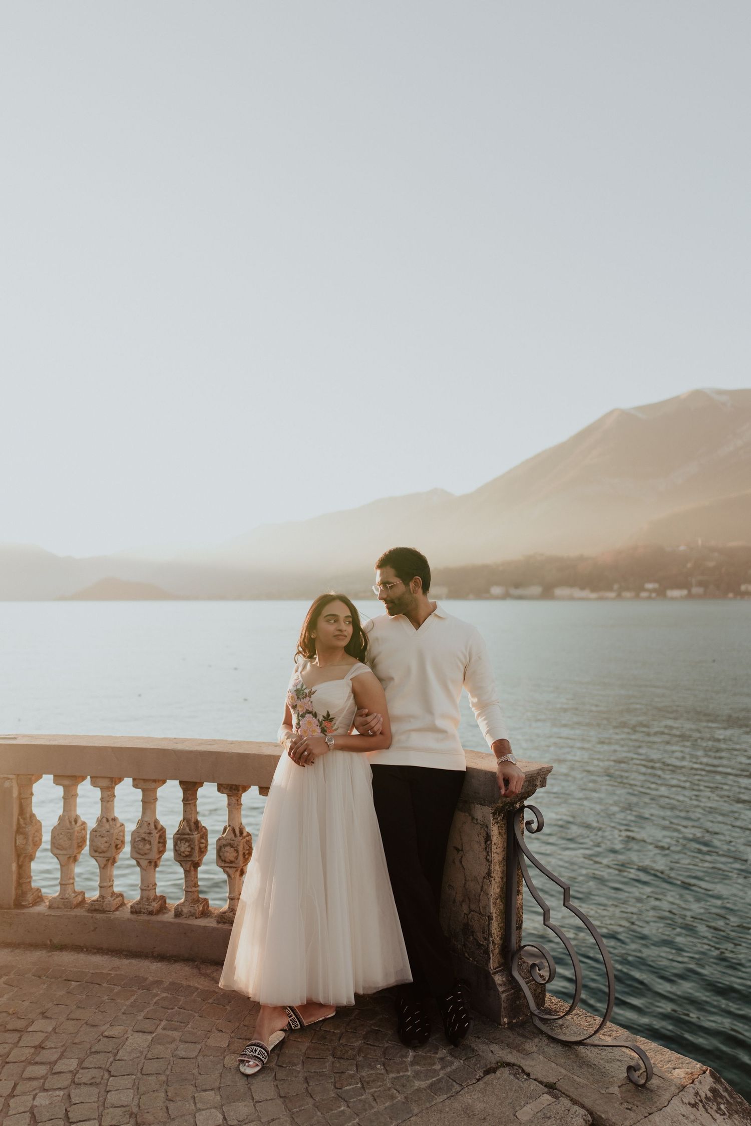 Elegant couple embracing on a lakeside terrace with mountain views at golden hour.