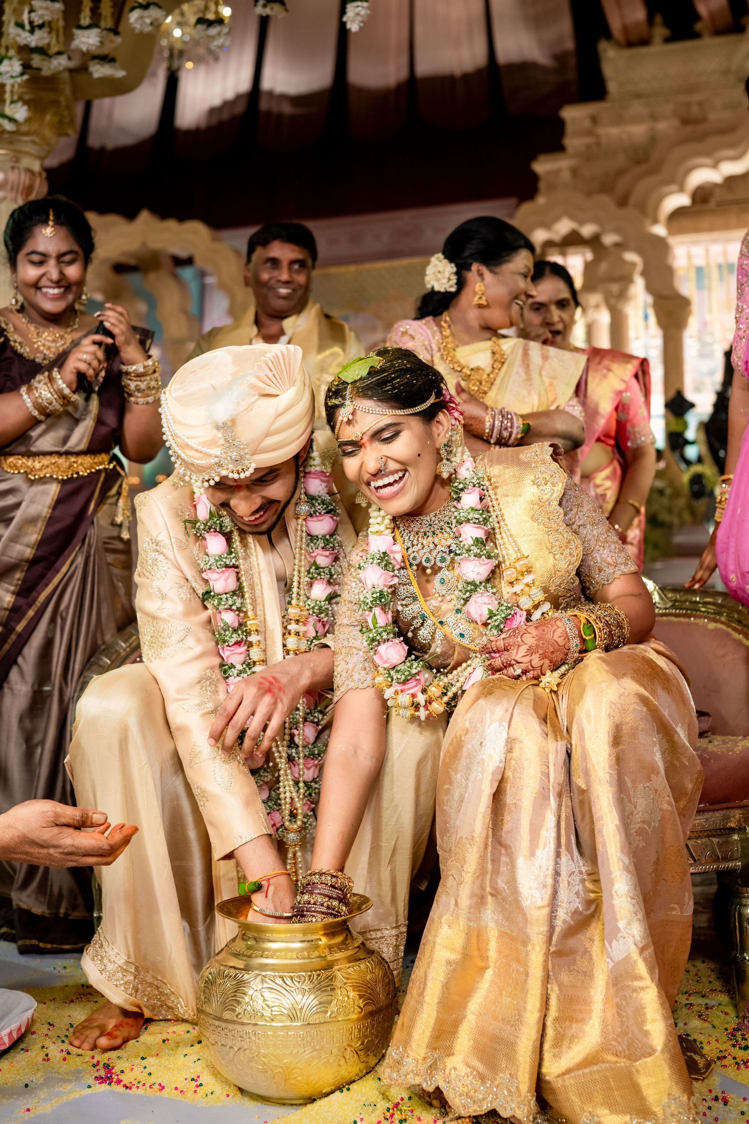 Bride and groom laughing together during traditional South Indian wedding ritual with gold pot.