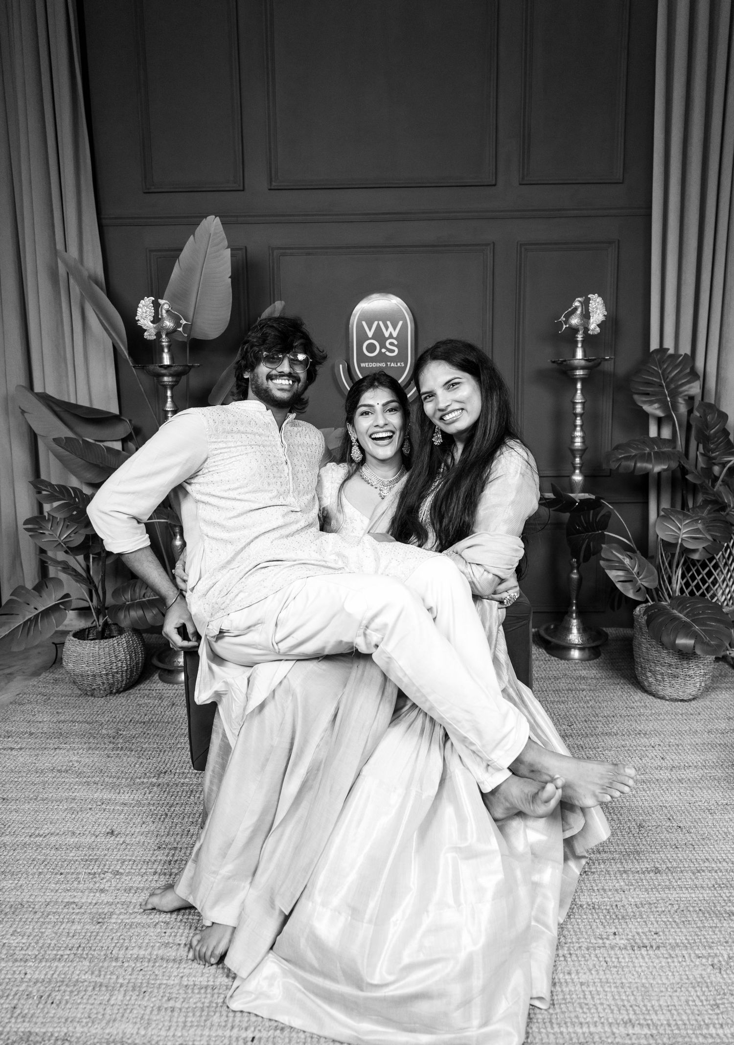 Black and white photo of three friends posing playfully, two holding one in the air, in a decorated indoor setting.