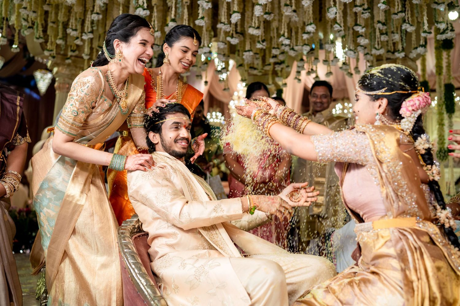Traditional South Indian wedding ceremony with bride and groom in gold silk attire, surrounded by joyful guests tossing flowers.