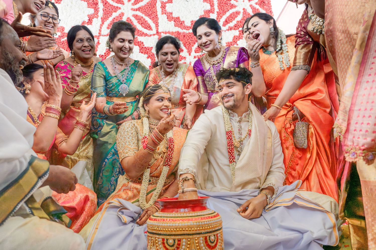 Joyful South Indian wedding ceremony with bride and groom seated, surrounded by smiling women in colorful silk sarees.