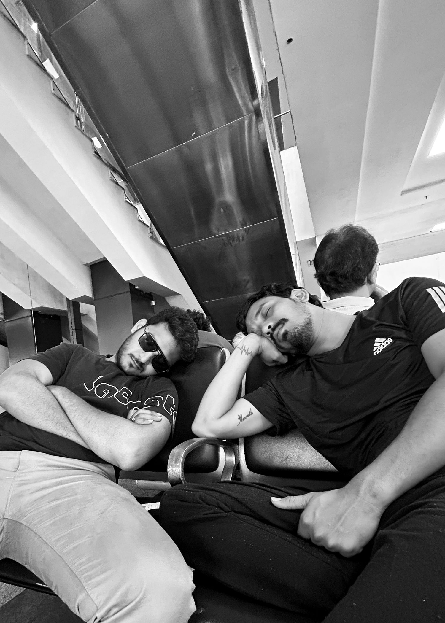 Two young men lounging together in black and white photo, one wearing sunglasses and the other an Adidas shirt.
