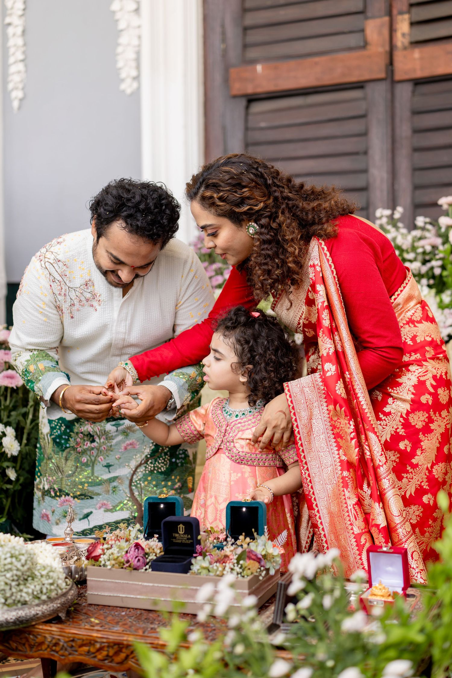 Indian family in traditional attire celebrating a festive ritual, with parents adorning their young daughter with jewelry.