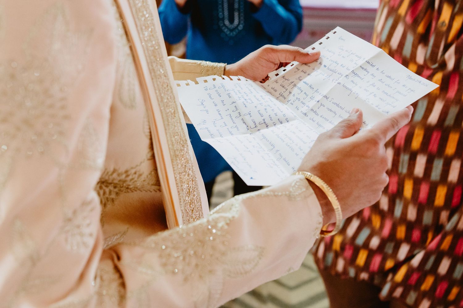 Bride in gold lehenga reading wedding vows document with gold bangles.