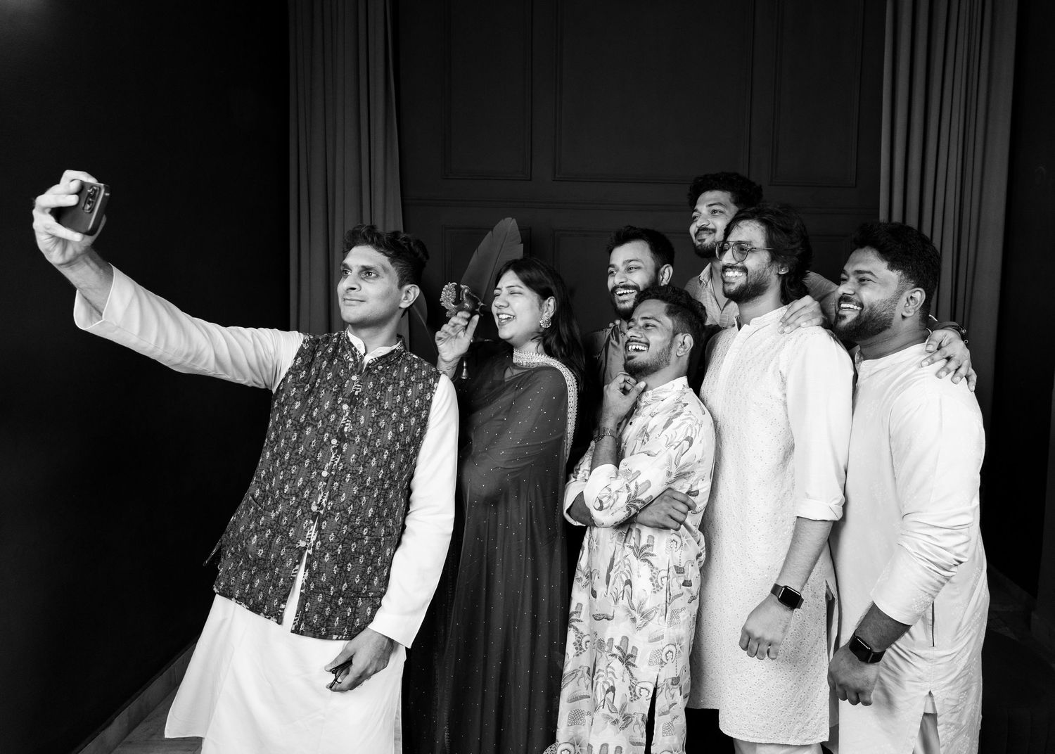 Group of friends in traditional Indian attire taking a joyful selfie together in black and white photo.