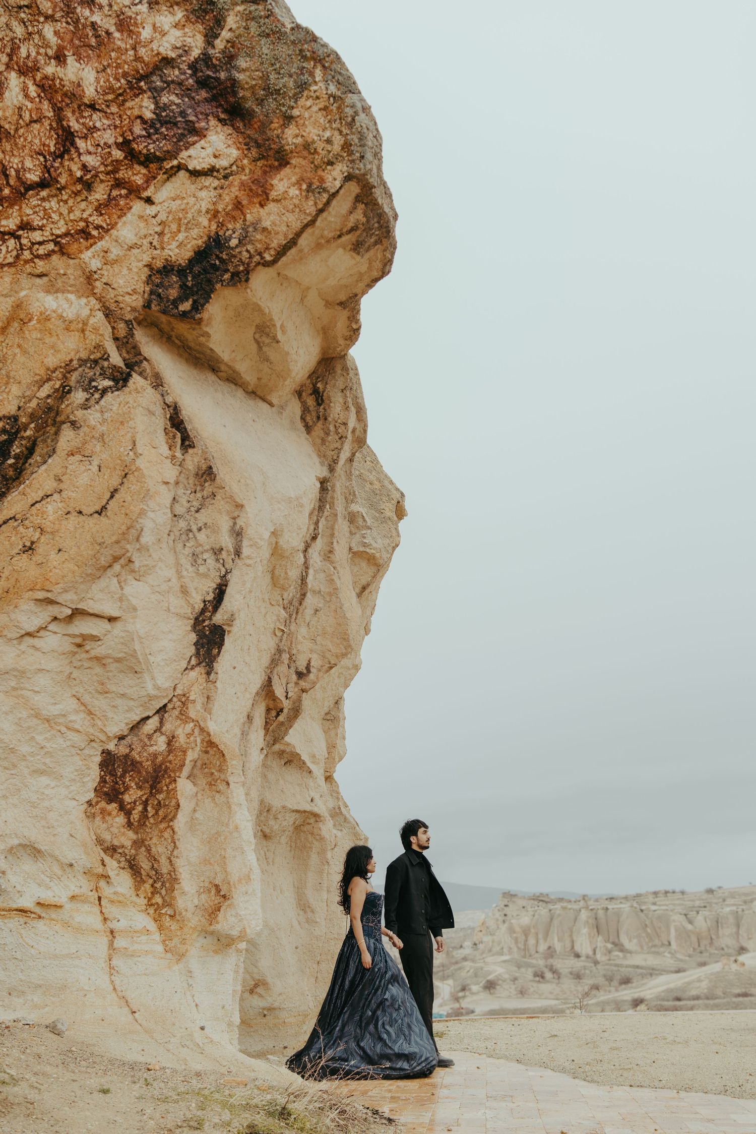 Couple in black attire posing by dramatic rock formations in Cappadocia, Turkey.