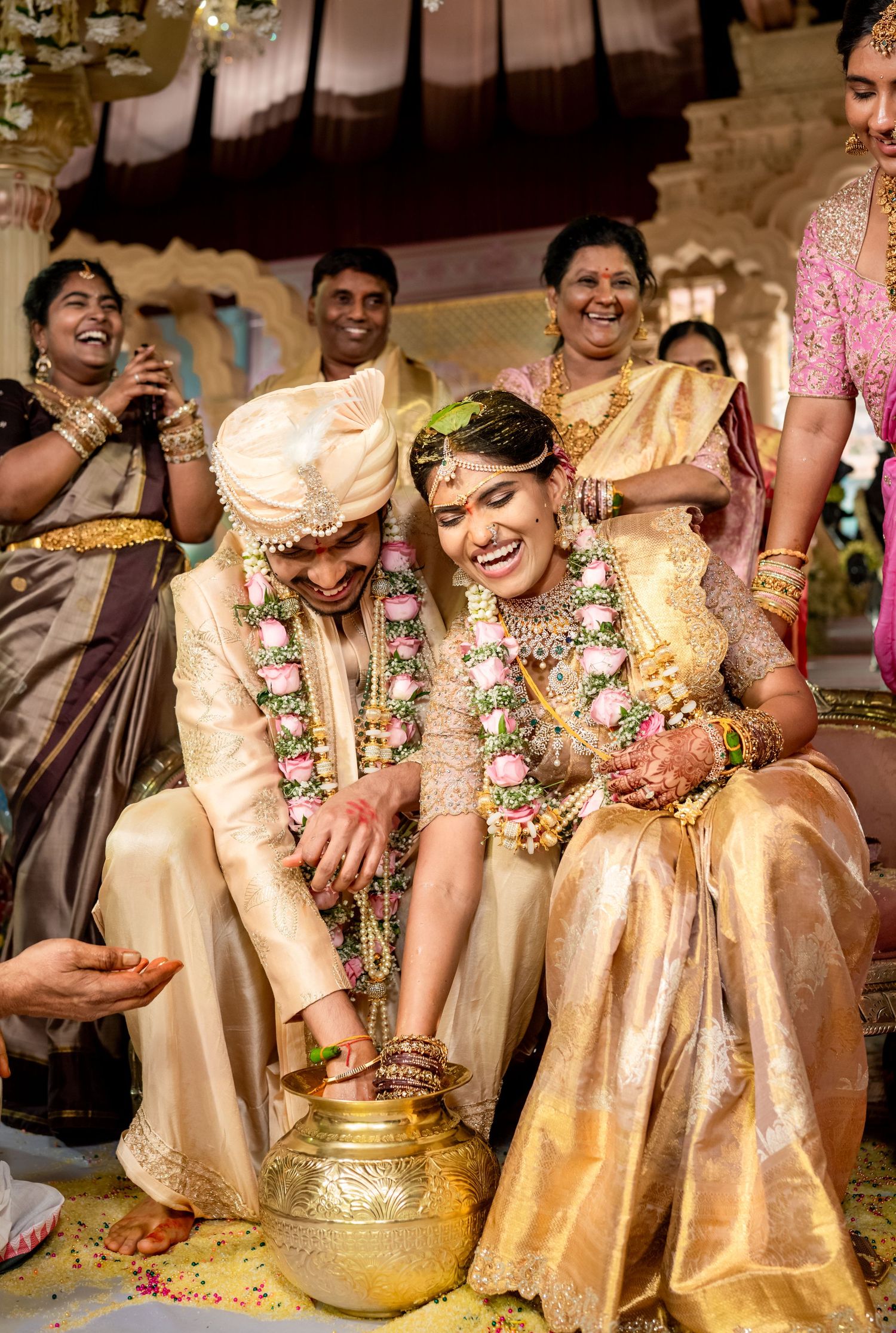 Joyful South Indian wedding couple in gold silk attire performing traditional ceremony rituals with flower garlands.