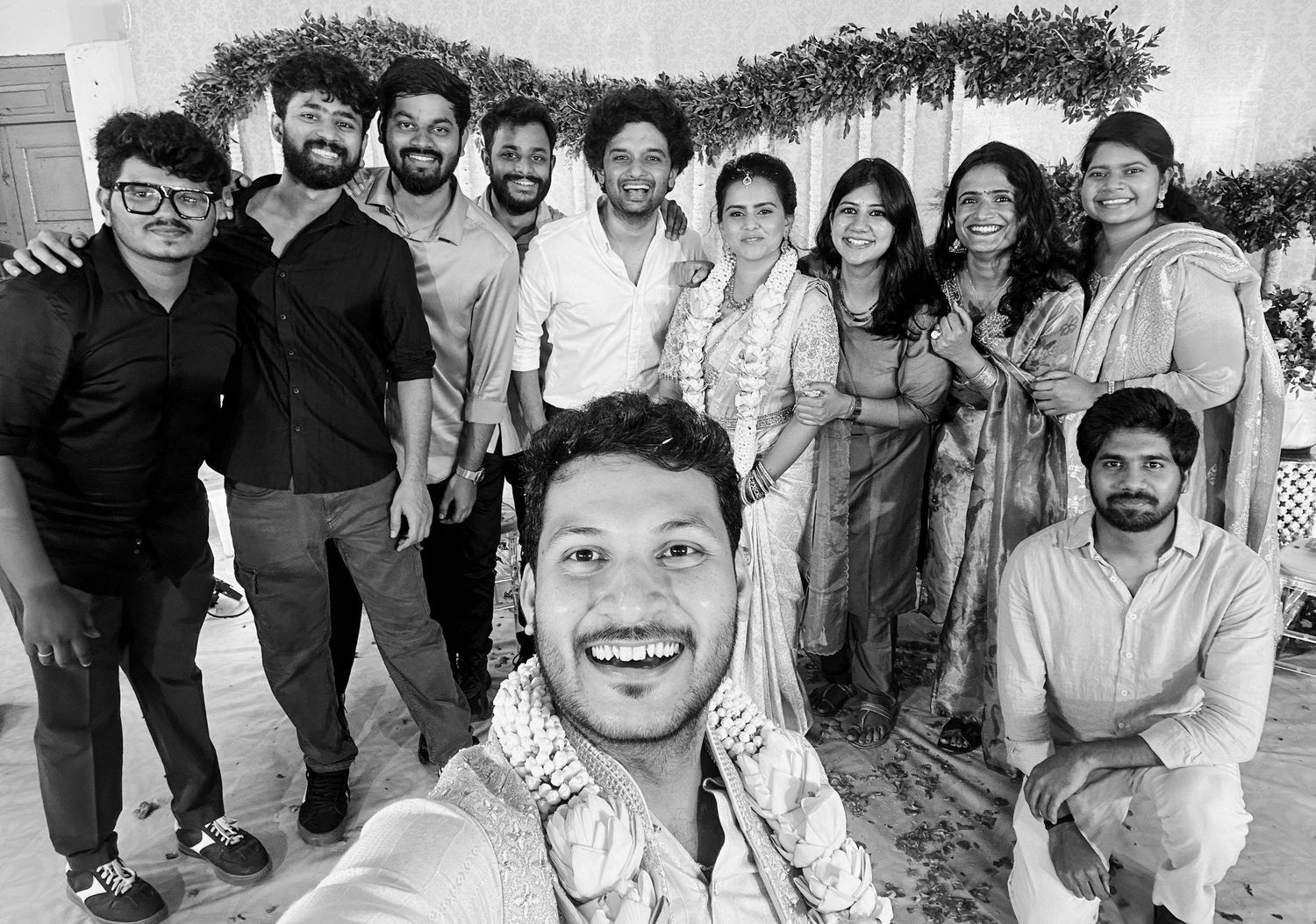 Black and white group selfie of smiling friends at an outdoor celebration or wedding event.