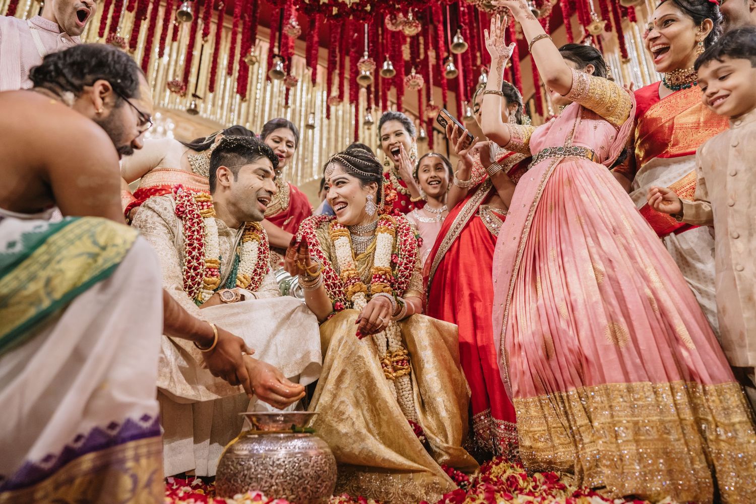 Joyful Indian wedding ceremony with bride in gold lehenga and groom in white, surrounded by celebrating guests in traditional attire.