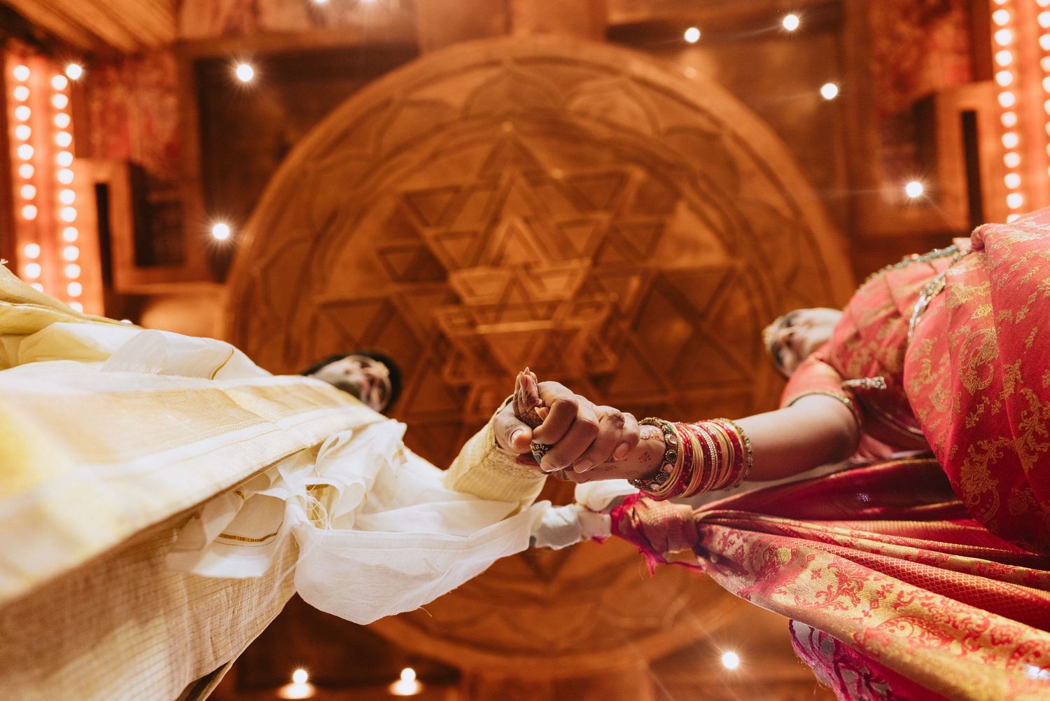 Indian wedding ceremony couple holding hands with henna mehndi designs, Star of David mandala backdrop with diya lights.