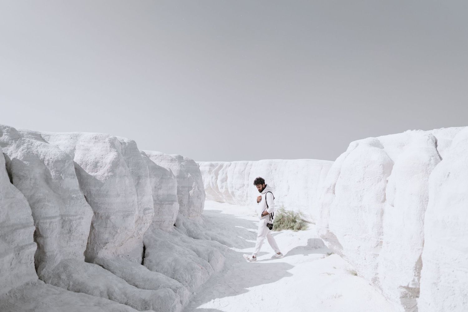 Person walking through white chalk rock formations in a bright, ethereal landscape.