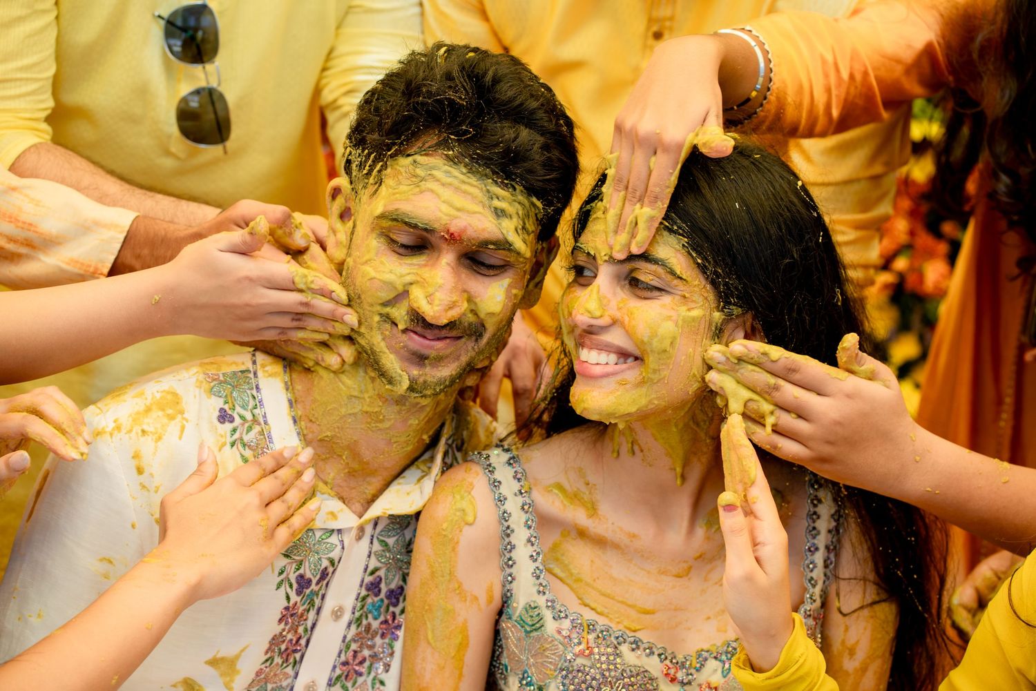 Couple joyfully covered in yellow turmeric paste during a traditional Indian Haldi wedding ceremony.