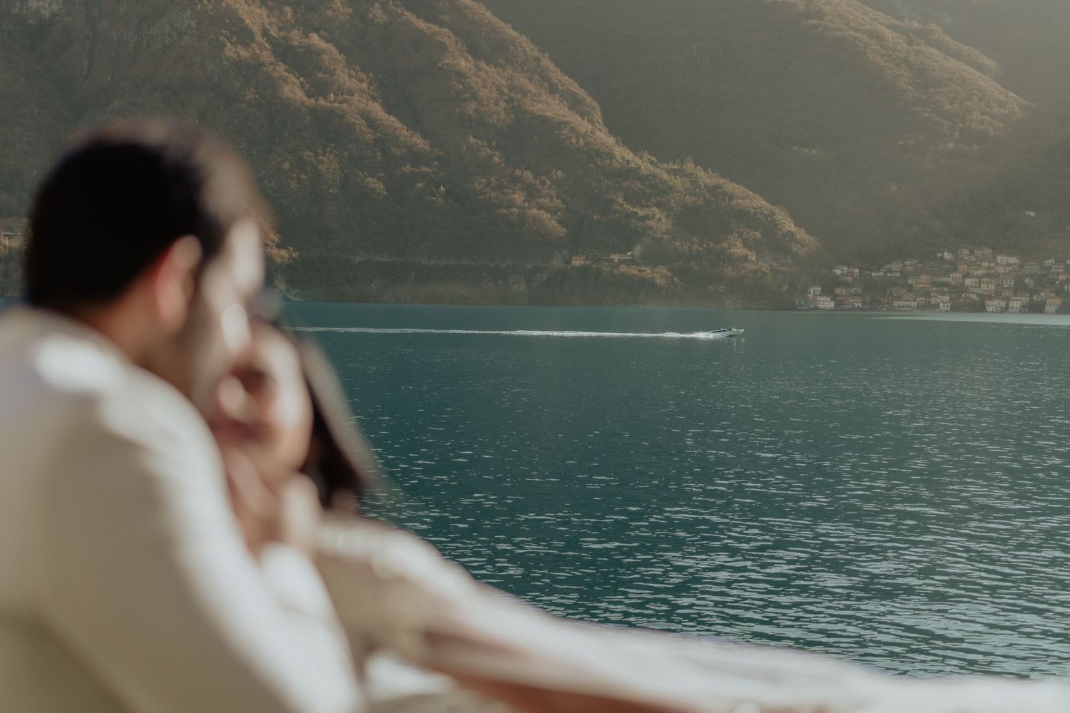 Couple sitting together on a boat enjoying scenic lake and mountain views on a sunny day.
