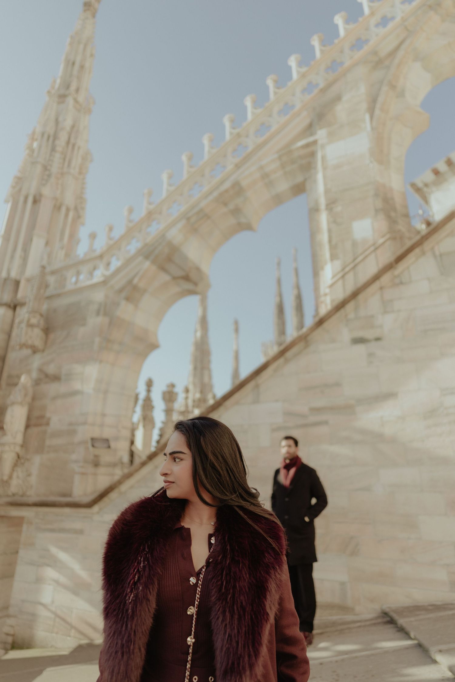 Elegant woman in burgundy fur coat standing before ornate Milan Cathedral marble architecture.
