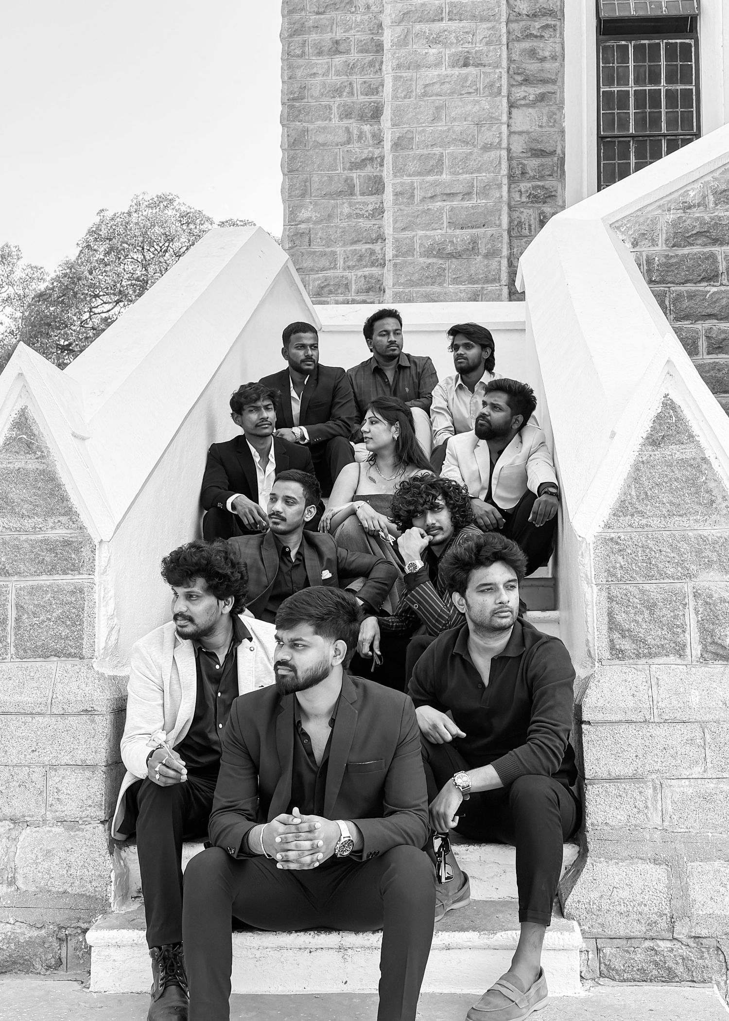 Group of young men and women posing on stone steps of a historic building in black and white photo.