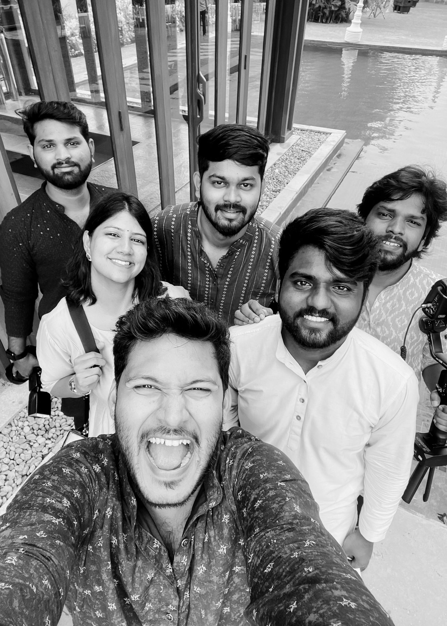 Black and white selfie of six smiling friends posing together outdoors near a water feature.
