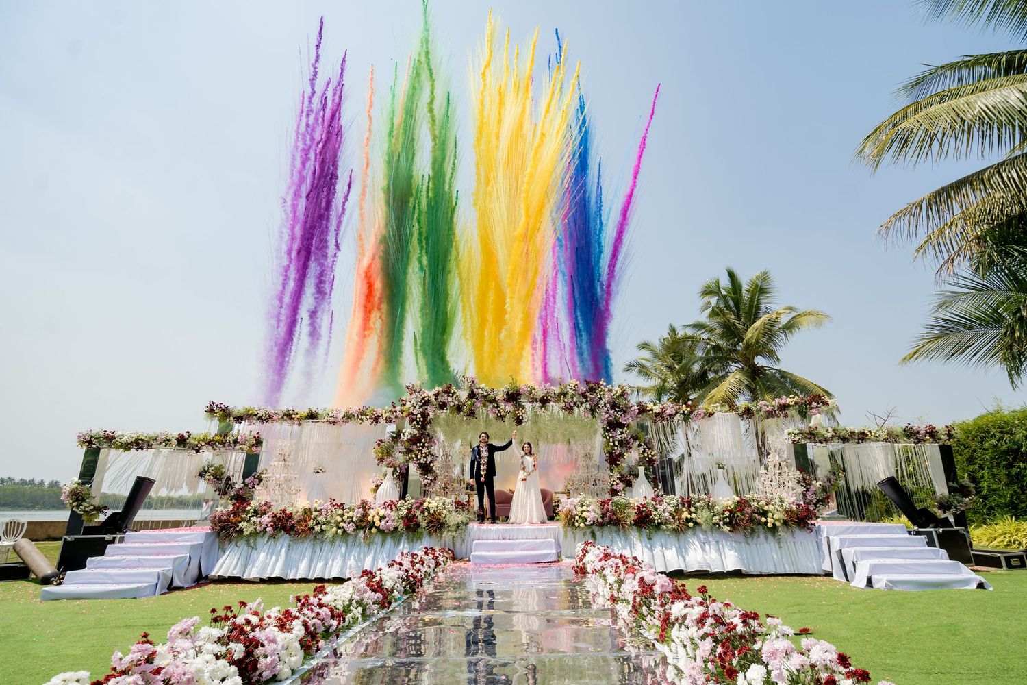 Colorful rainbow ribbon wedding ceremony backdrop with floral aisle decorations at an outdoor venue.