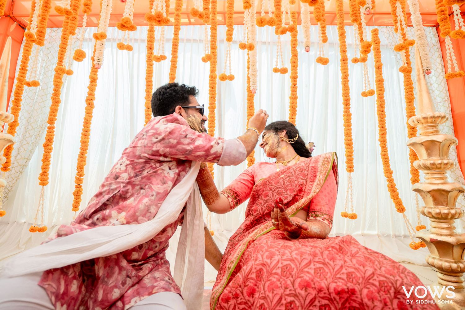 Bride and groom in traditional red Indian wedding attire during a vibrant Hindu ceremony with marigold decorations.