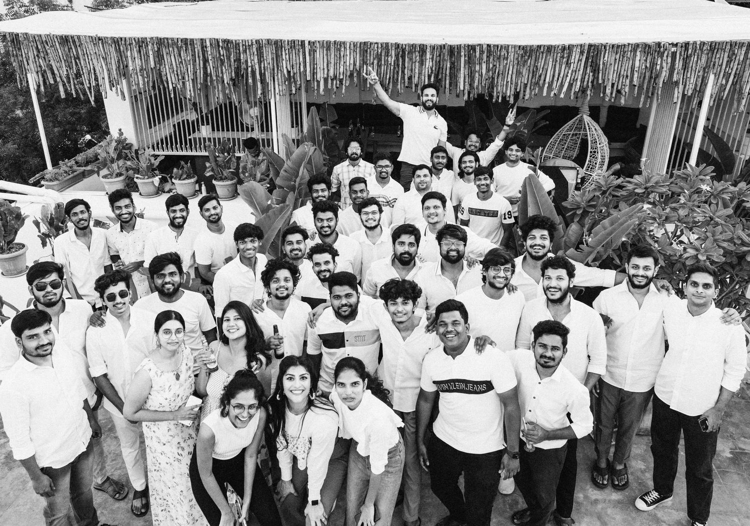 Large group of smiling professionals posing outdoors for a black and white team photo at a tropical venue.